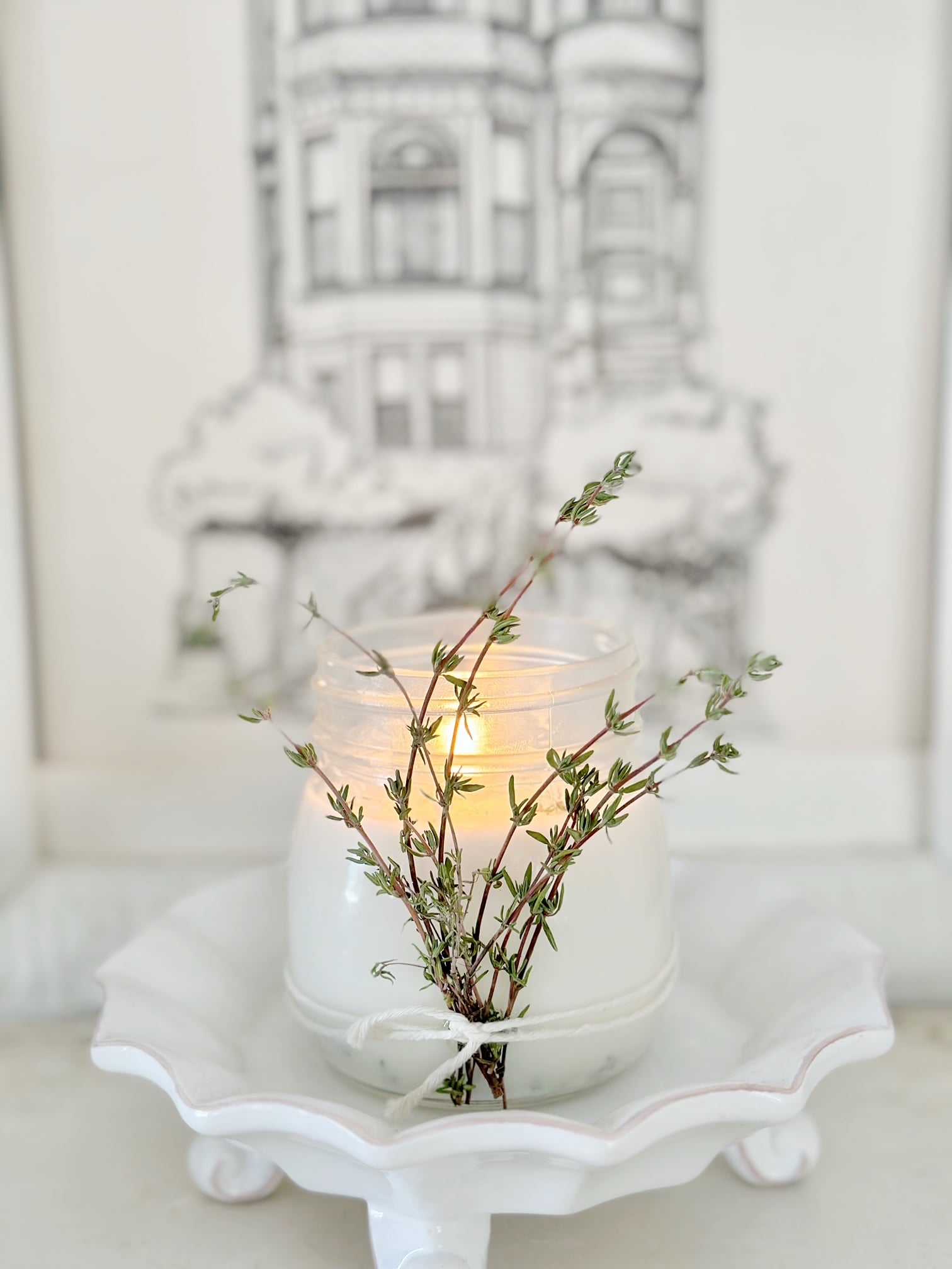 Thyme candle in front of a black and white print of an old house.
