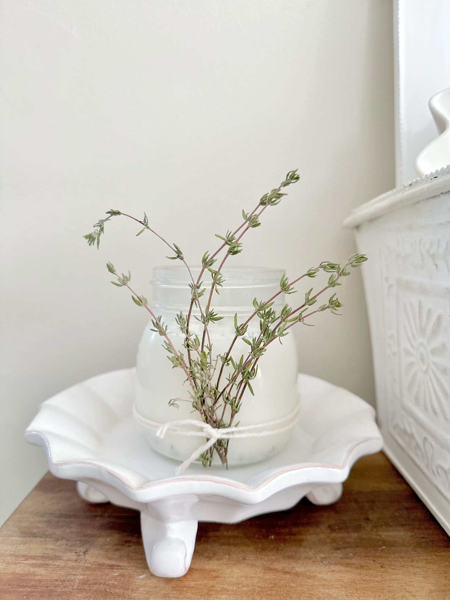 A pretty DIY Thyme Candle on a white dish. 