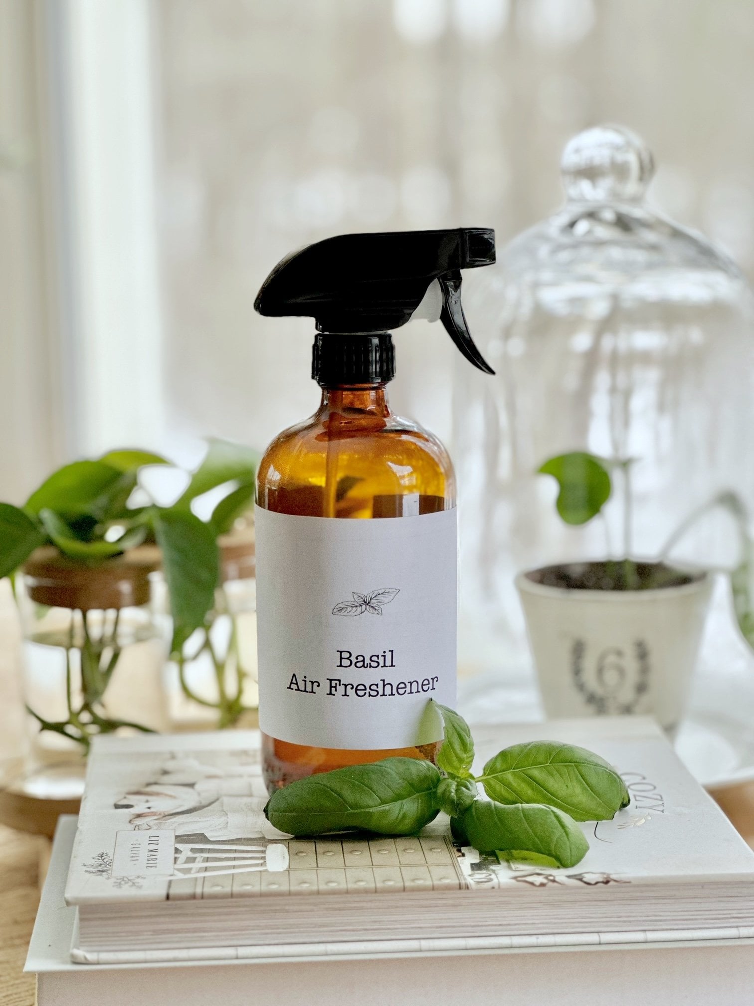 The basil air freshener spray bottle with plants in the background. 