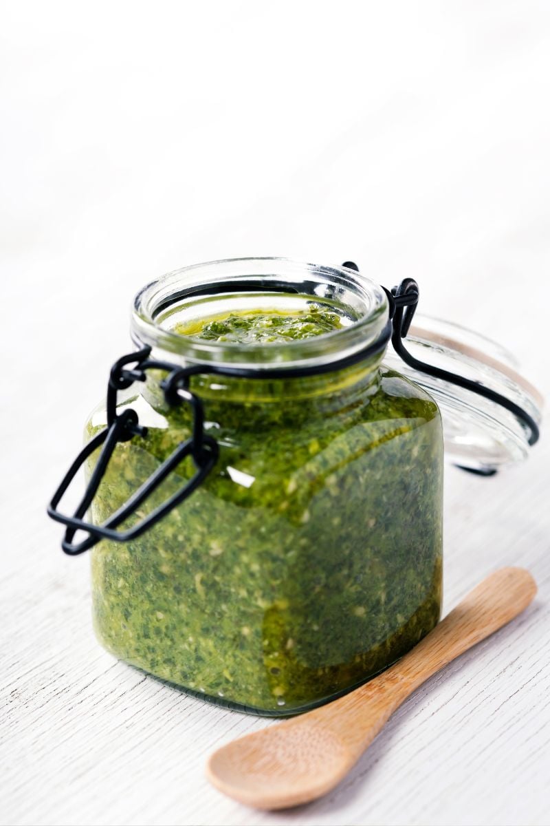 Basil pesto in a jar with a wooden spoon. 