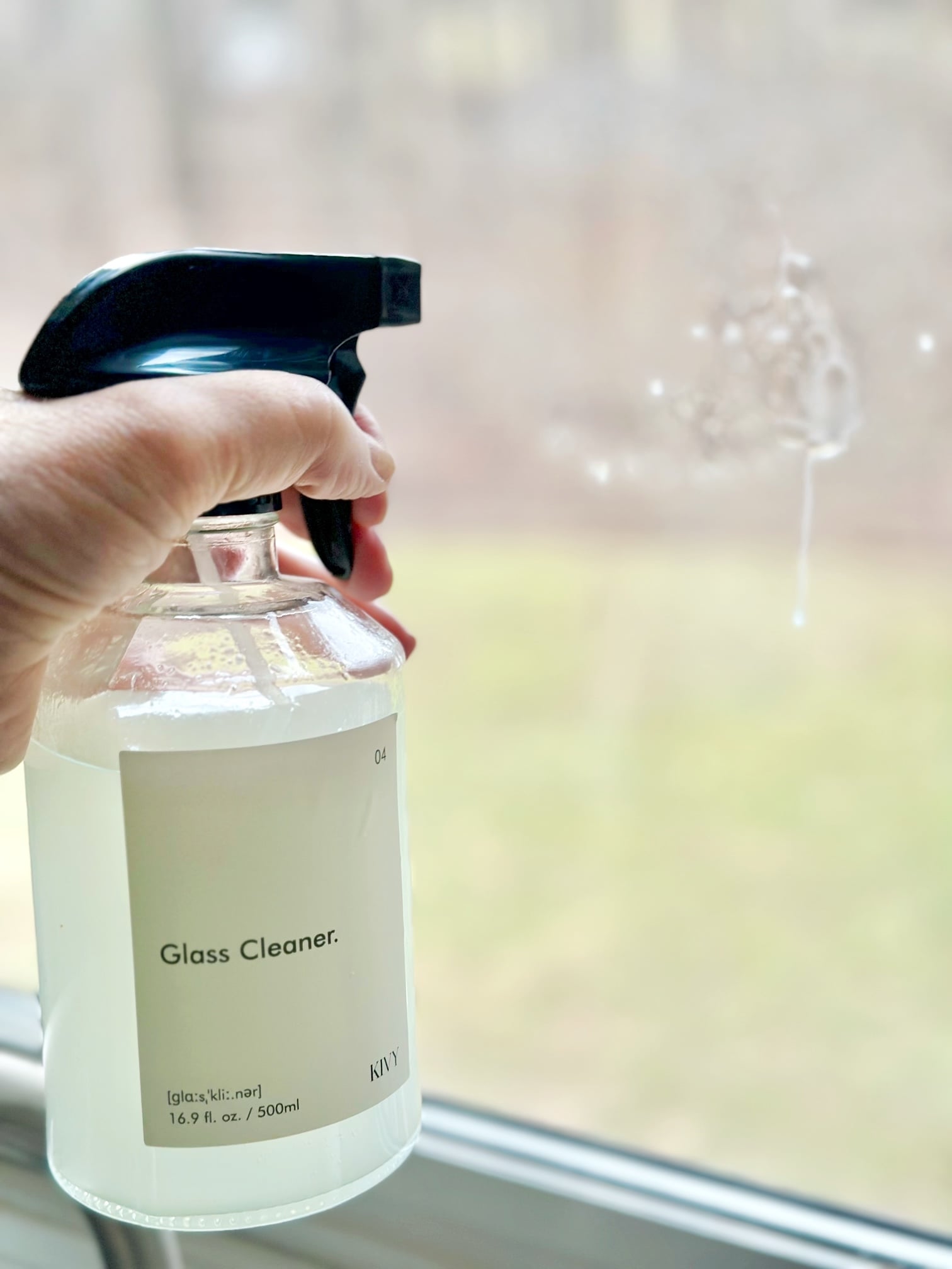 All natural glass cleaner in a spray bottle spraying a window.