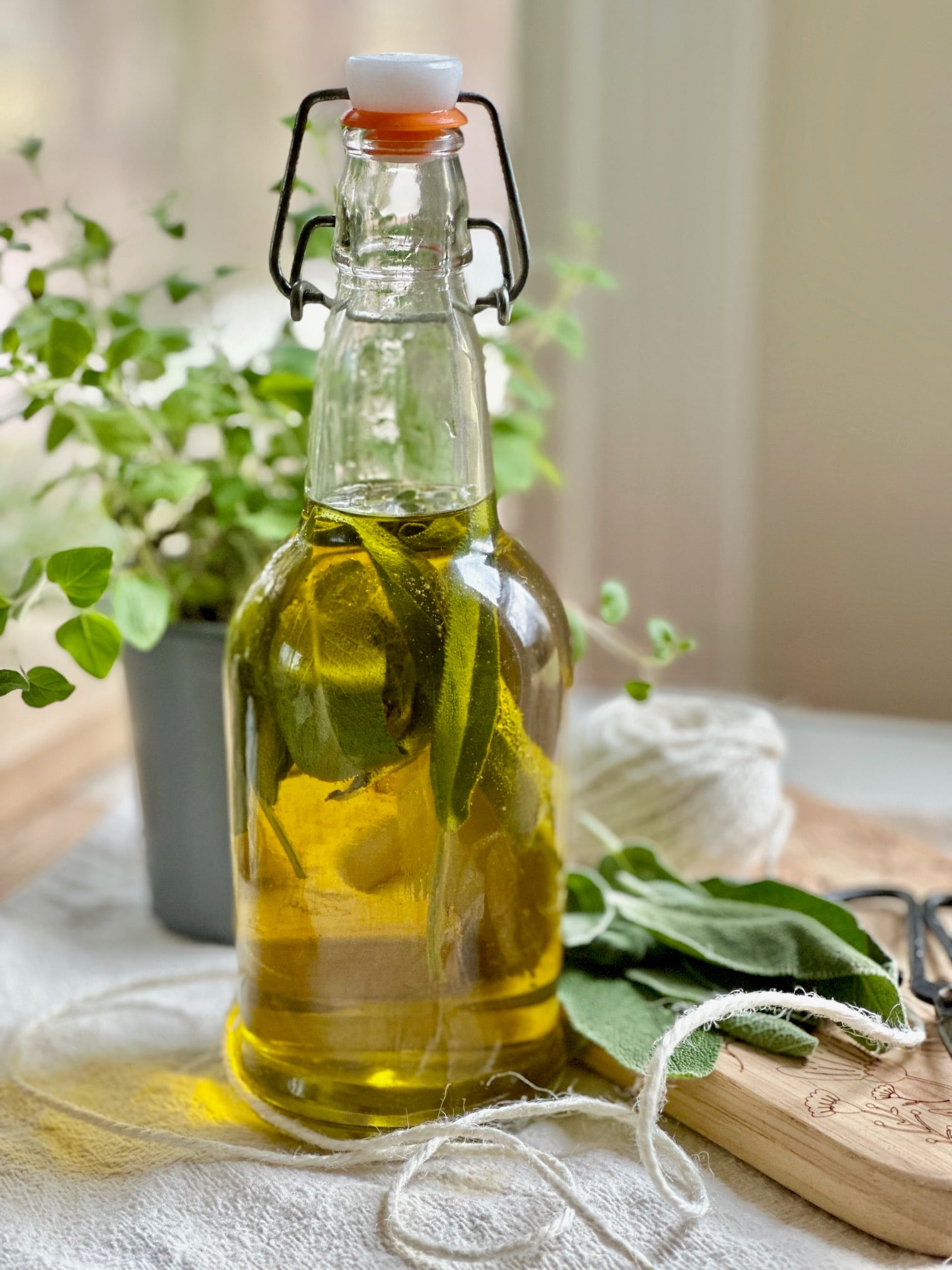 Sage oil in a glass bottle with a sage bundle on a cutting board. 