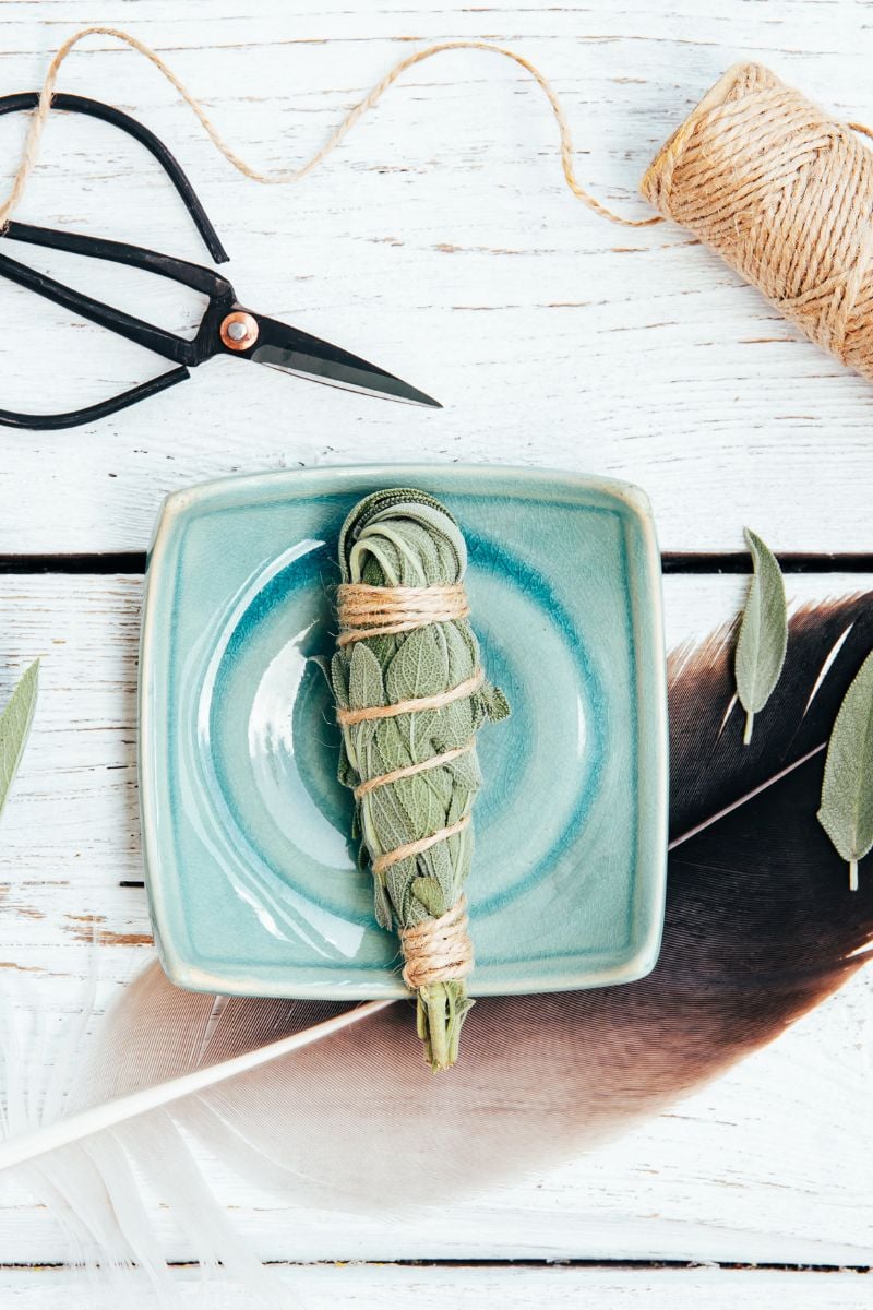 A sage smudge stick on a dish, scissors and twine.