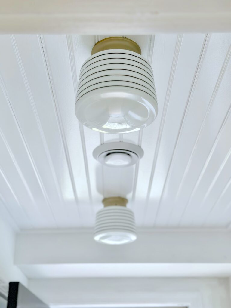 The beadboard ceiling painted white with two striped globe lights. 