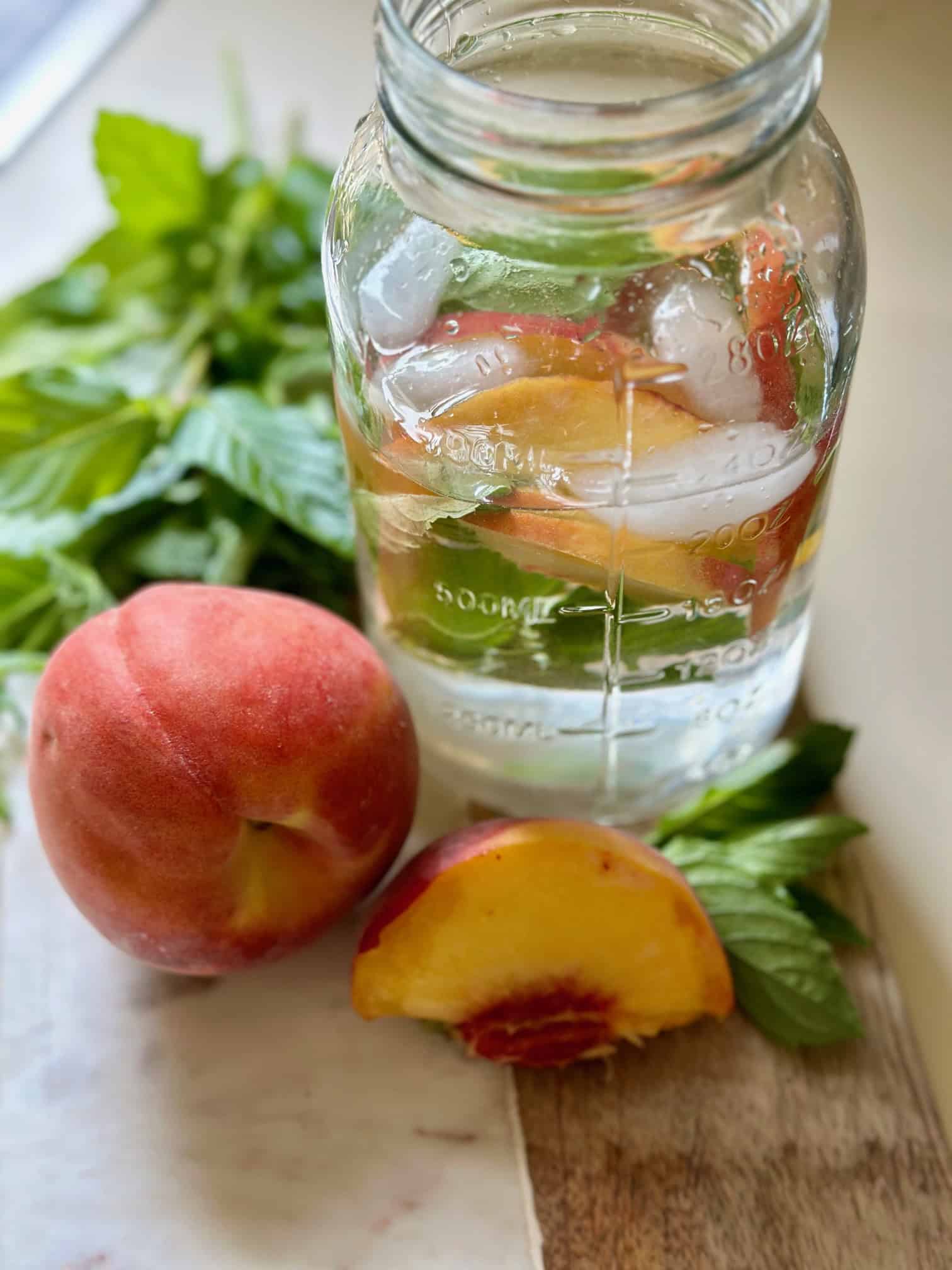 A large ball jar filled with peaches and mint leaves.