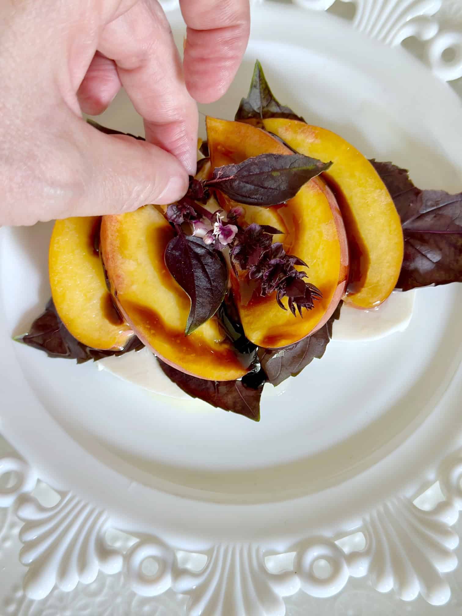 Placing a purple basil flower on a stack of peaches. 