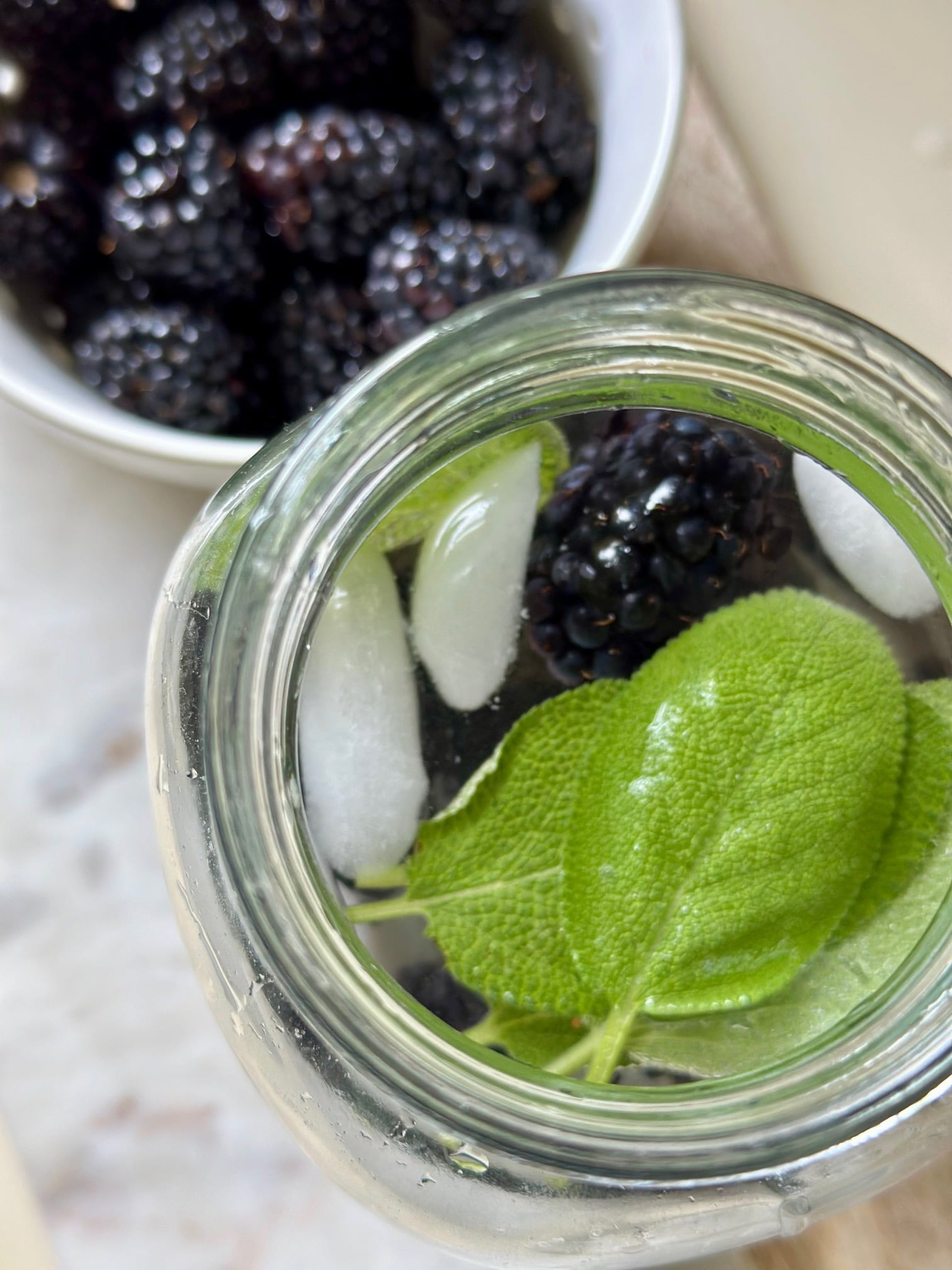 blackberries with sage leaves in a glass of ice water.