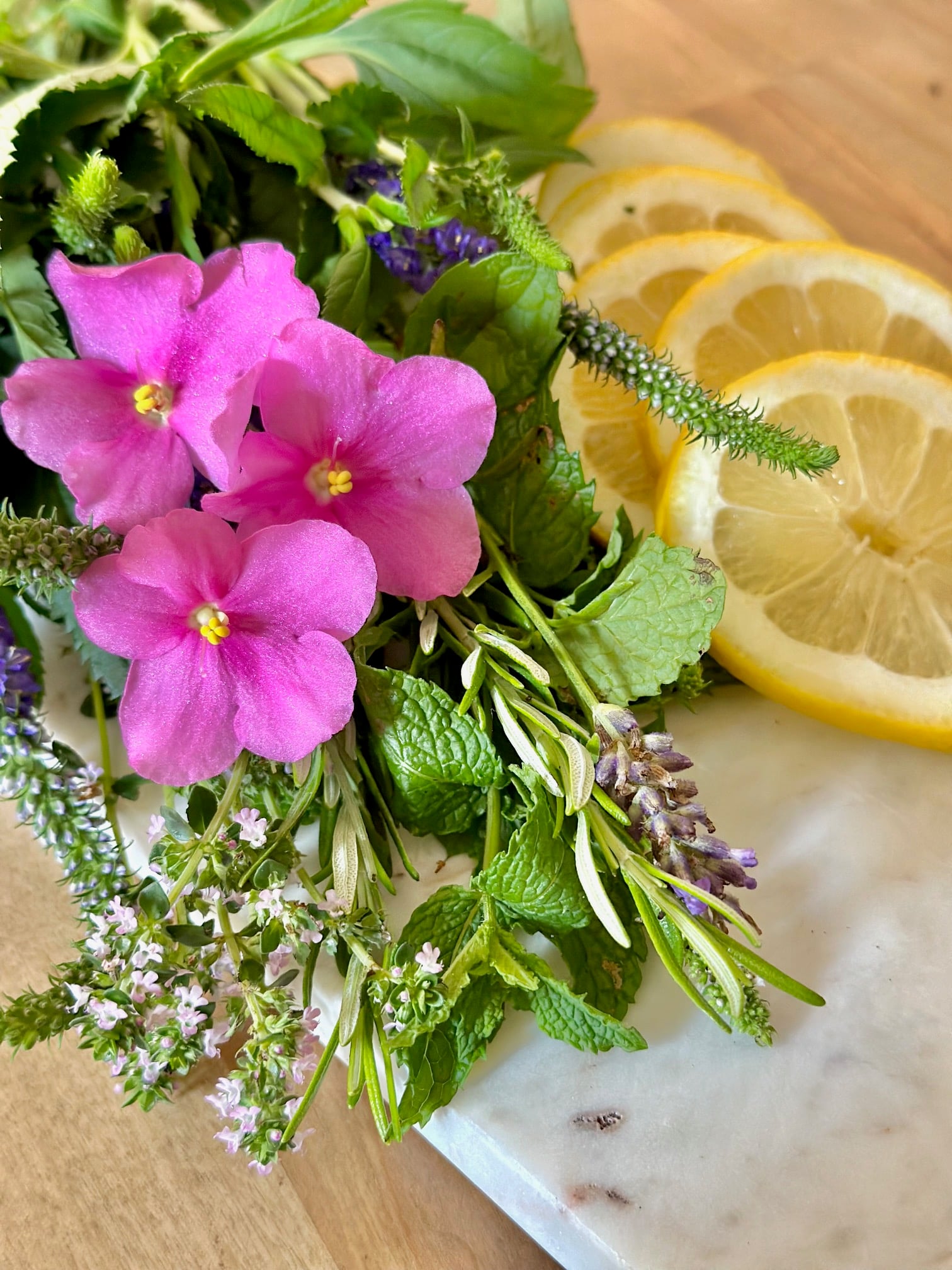 flowers, herbs and sliced lemon on a cutting board.