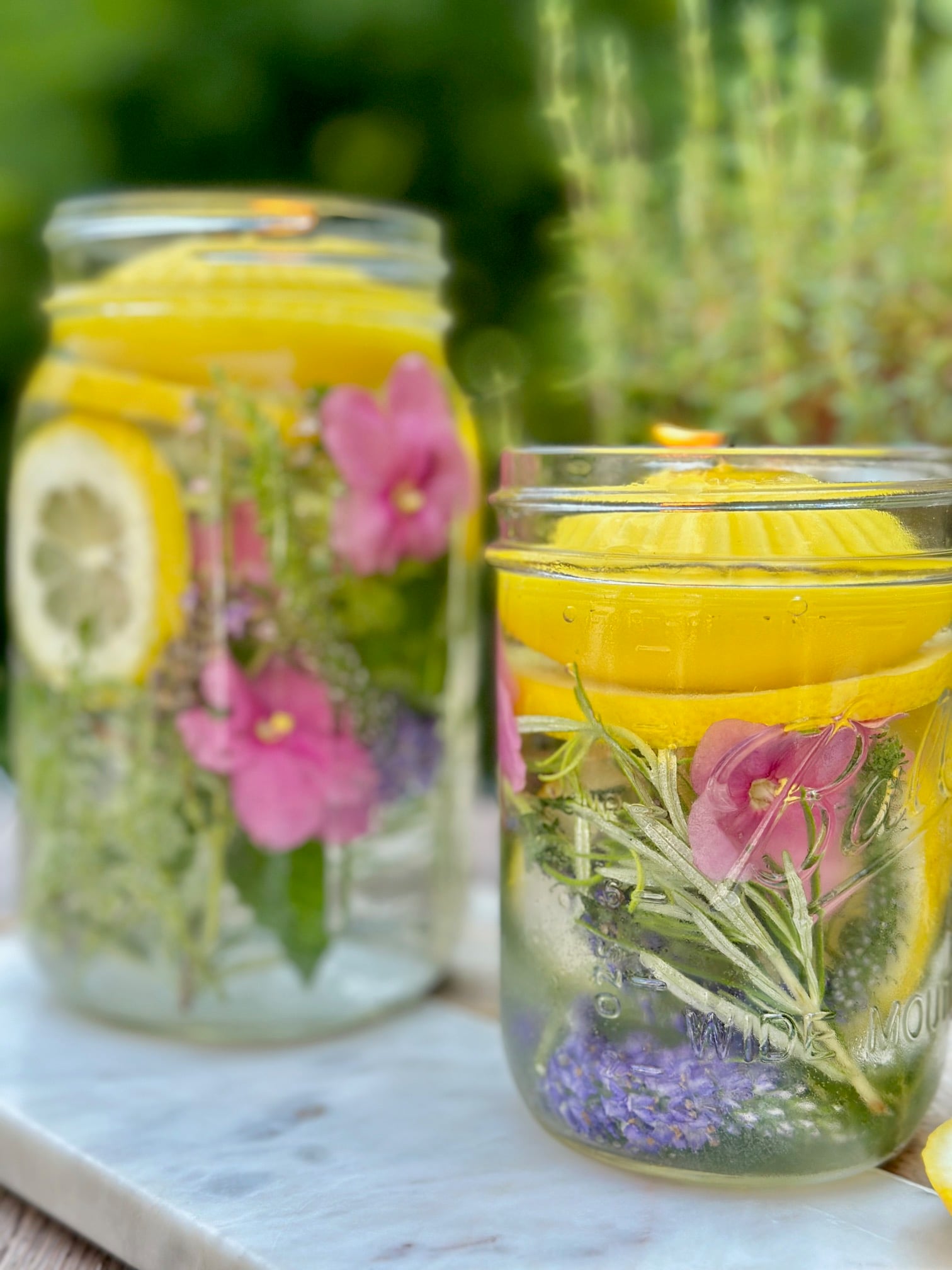 jars filled with herds and colorful flowers. they have a yellow citronella candle floating on top.