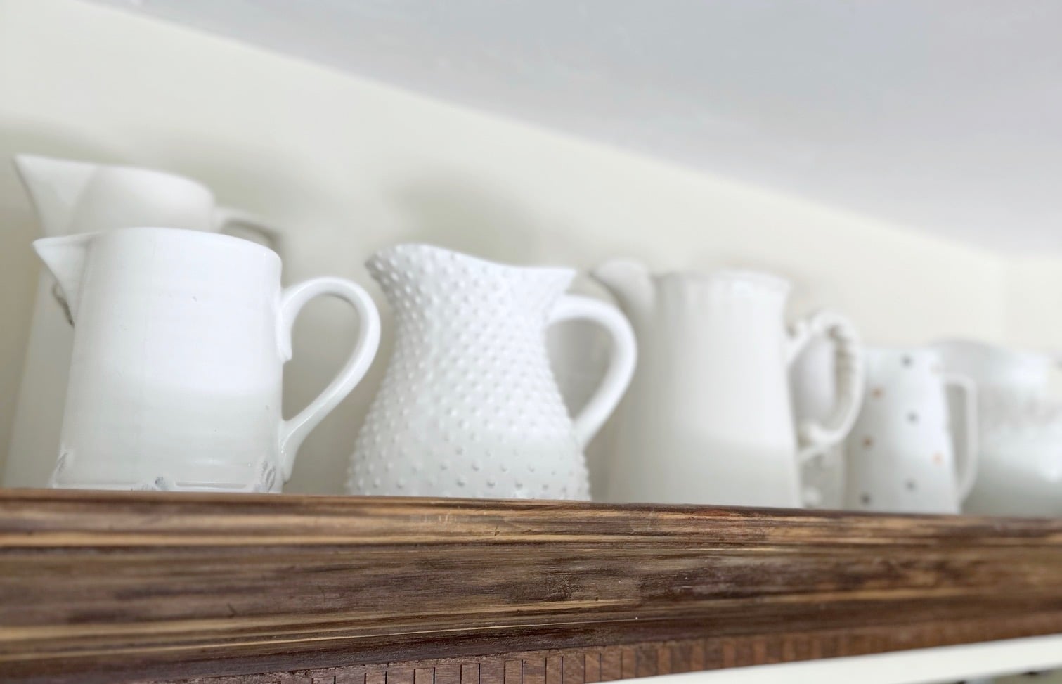 White assorted pitchers lined up across the top of the hutch.
