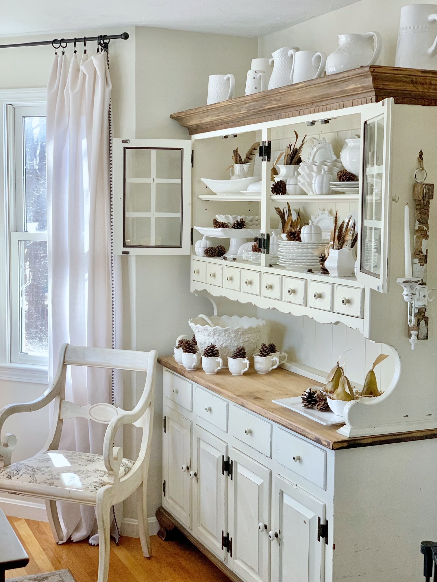 A full view of a fall decorated hutch using pinecones, fathers and pears.