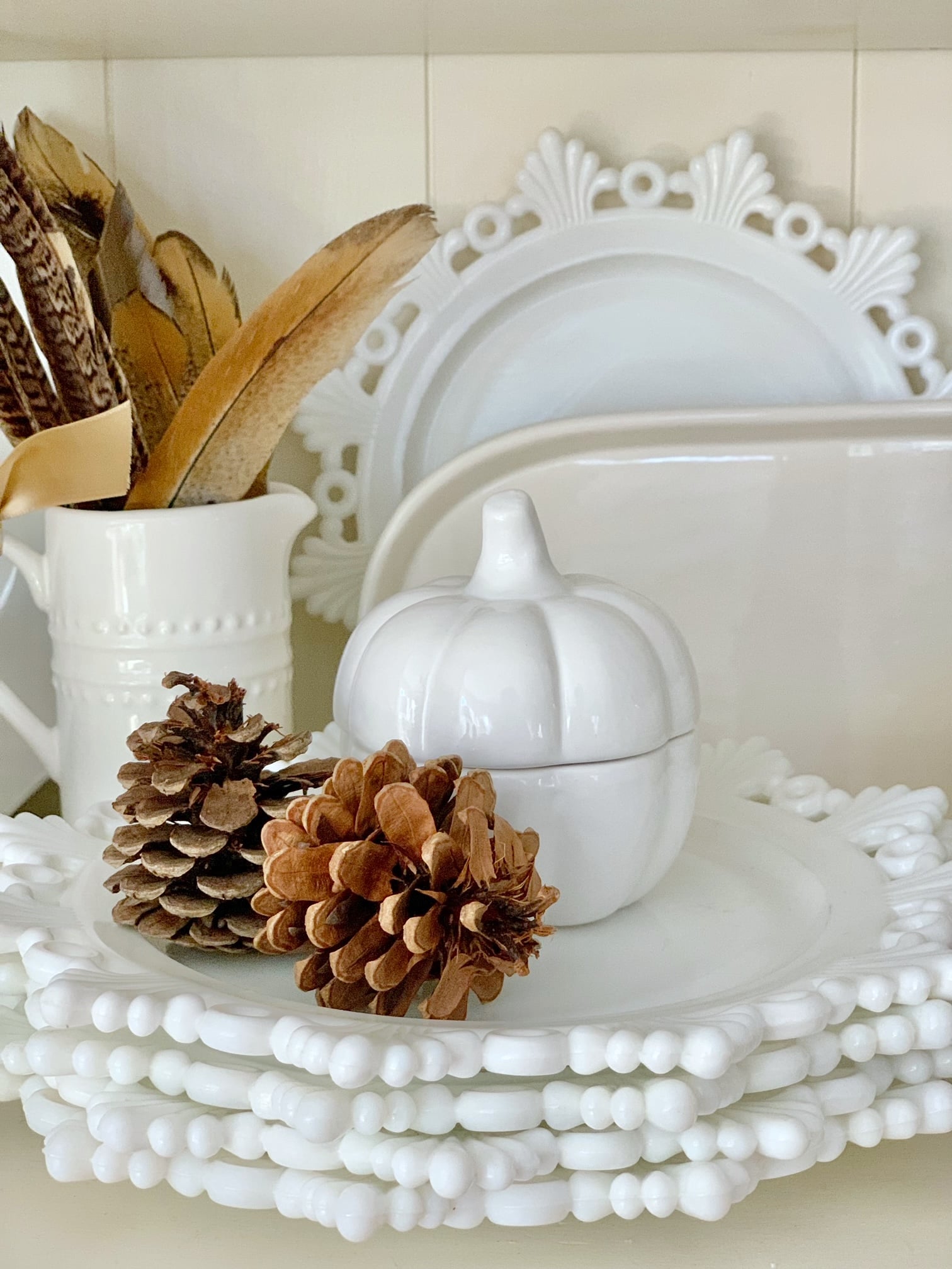 Dishes stacked with a ceramic pumpkins and pine cones.