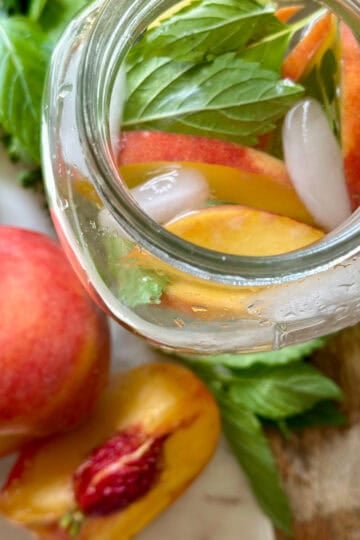 Beautiful peaches with herbs in a jar of infused water.
