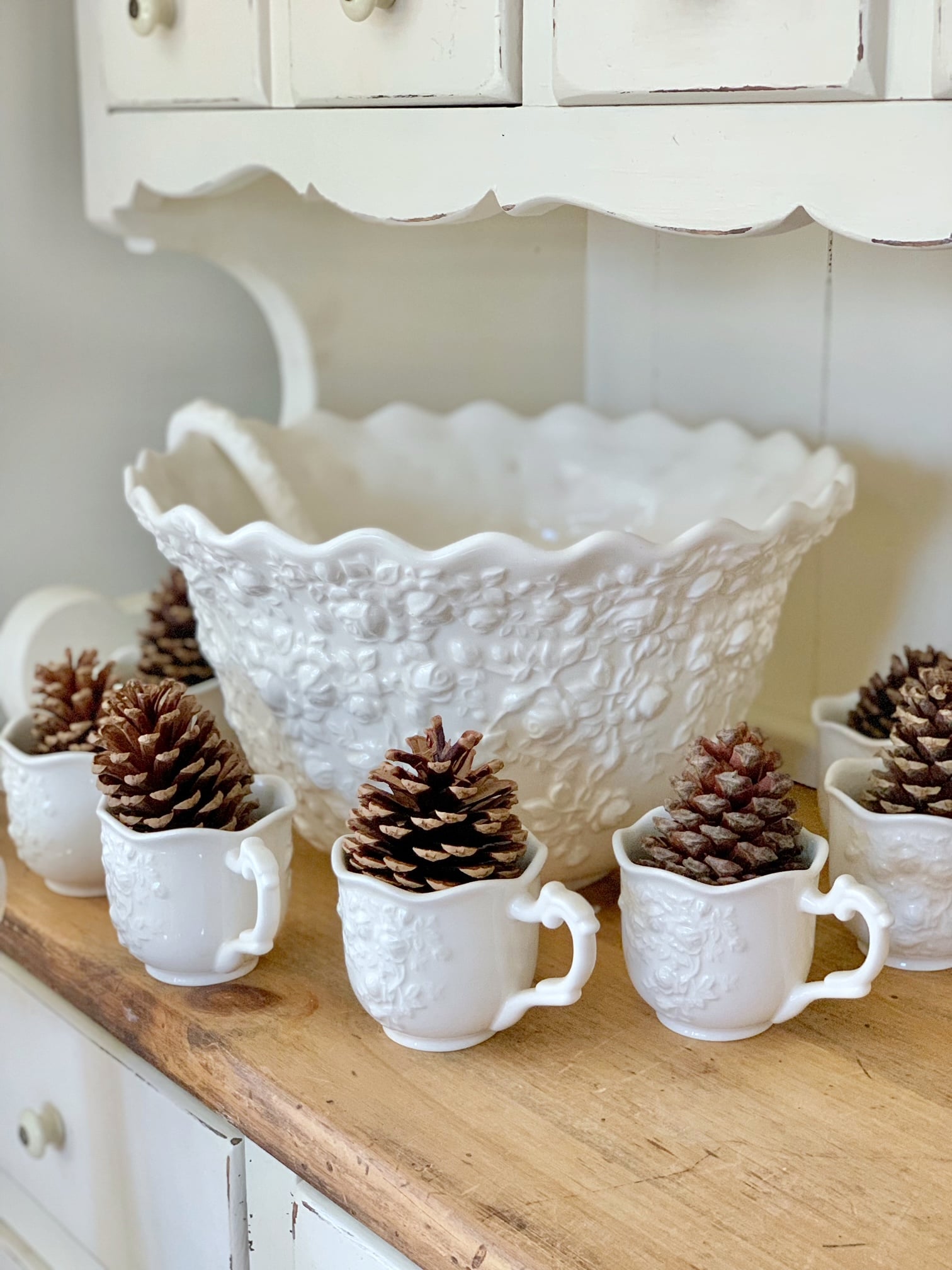 A large off-white floral embossed punch bowl with pinecones in the cups.