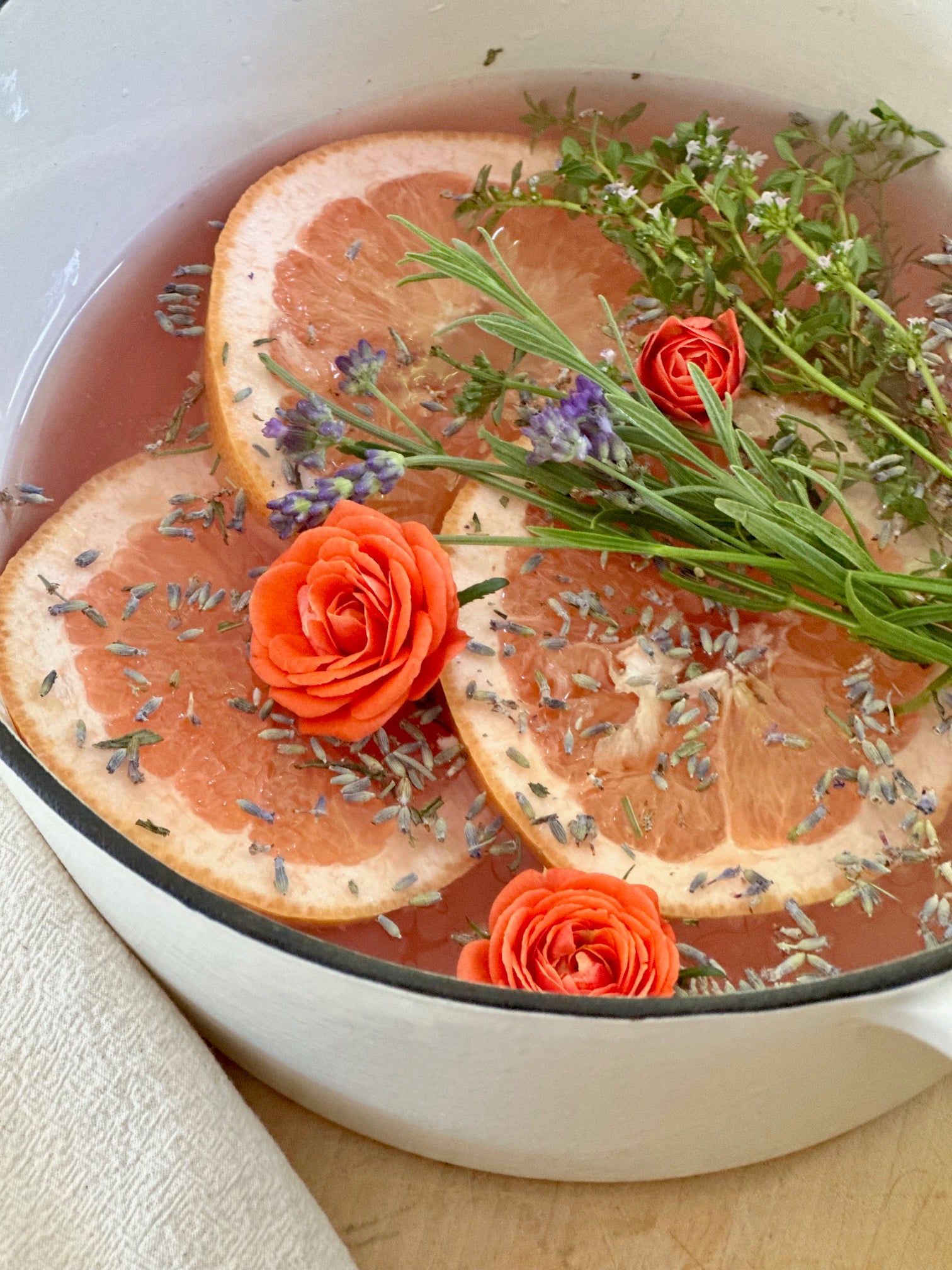 Grapefruit slices, lavender stems and buds, orange roses and thyme floating in water in a white dutch oven.