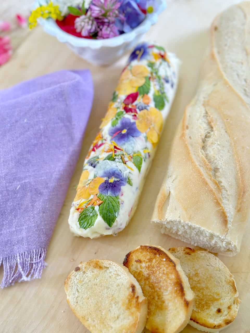 Napkin, butter, bread and a bowl of flowers on a cutting board.