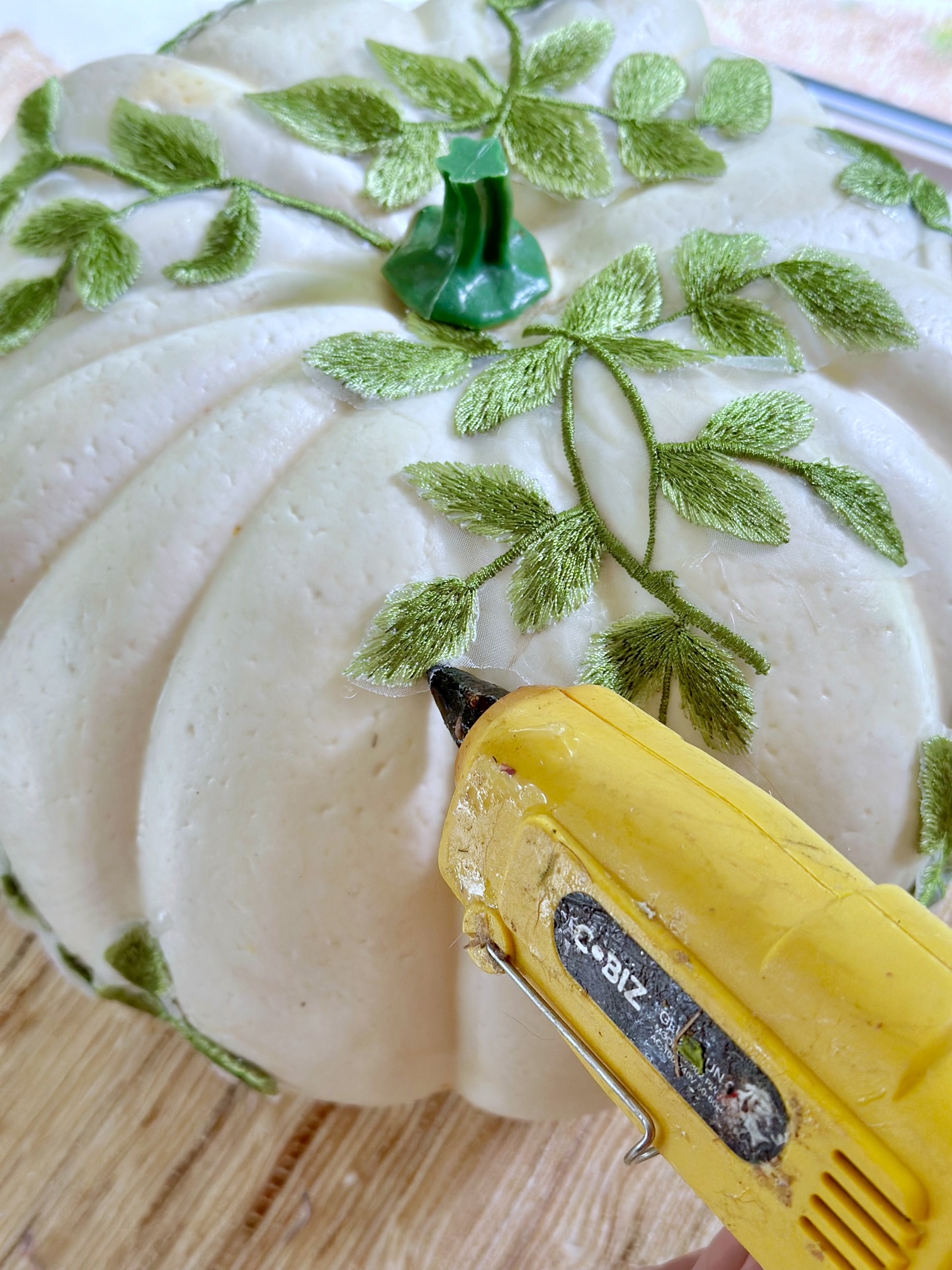A glue gun gluing leaves on a white pumpkin. 