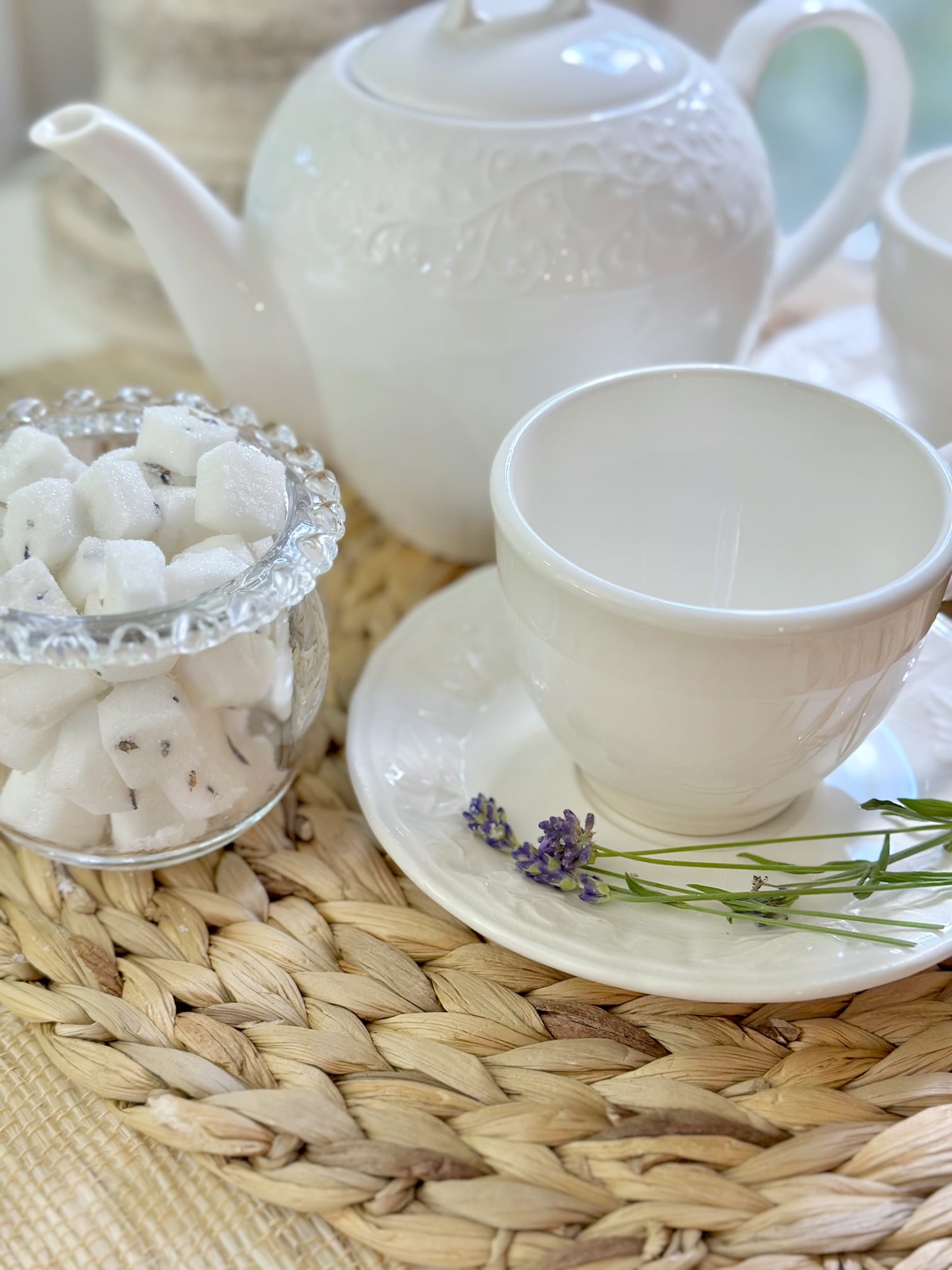 A tea set up with tea pot, white tea cup and lavender sugar cubes. 