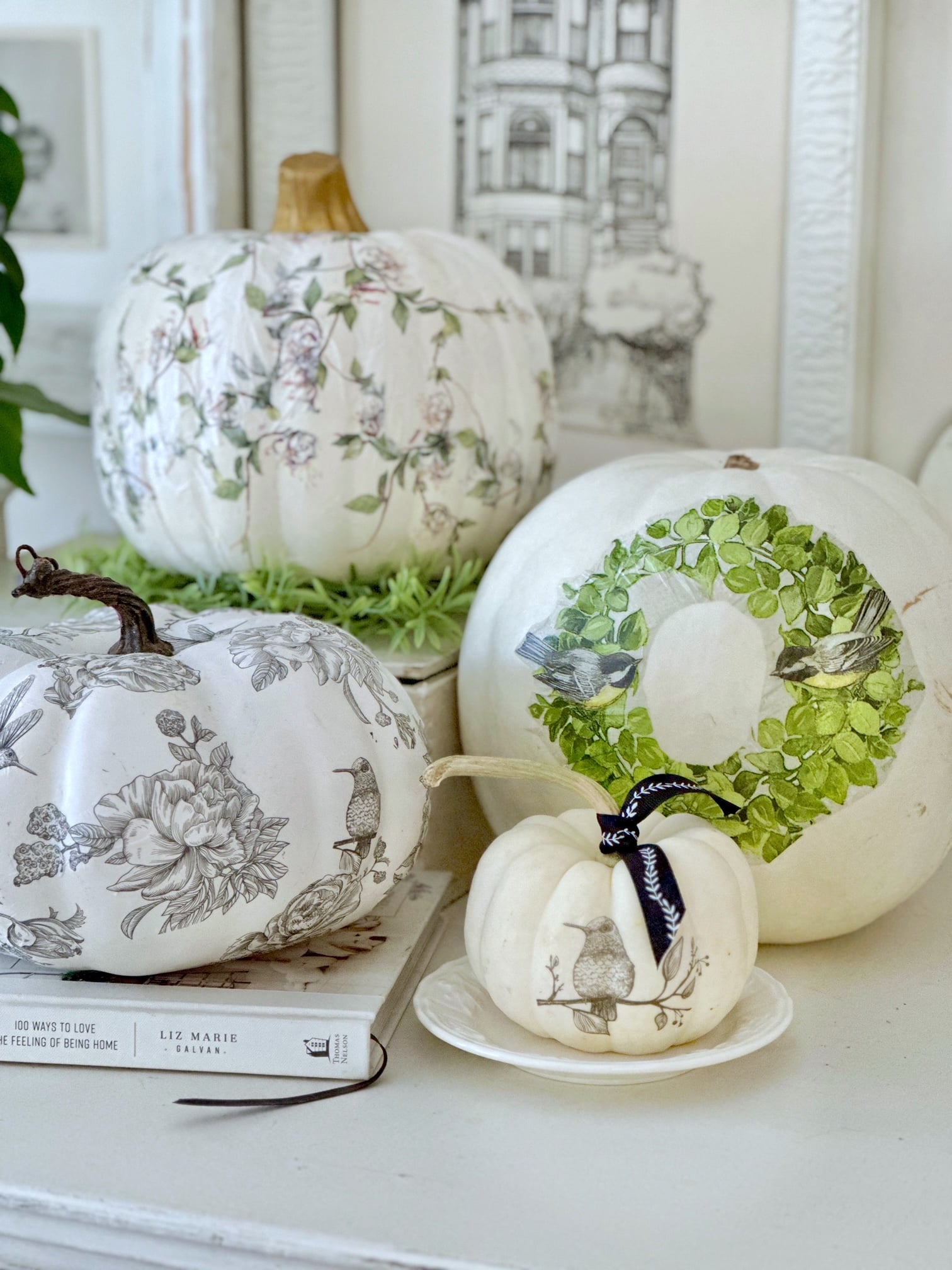 4 white decoupage pumpkins sitting in front of a gallery wall. 