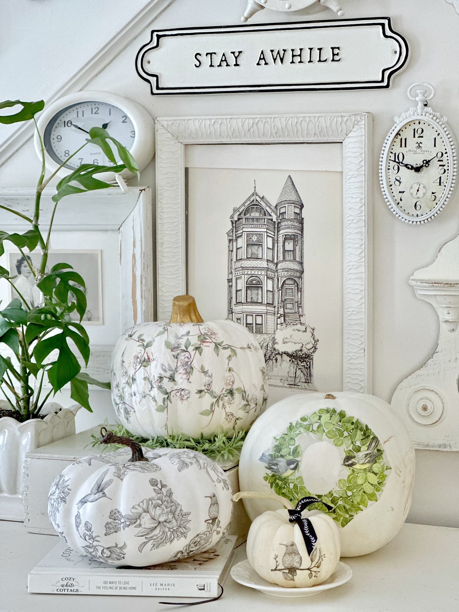3 styles of decoupage pumpkins. All on the theme of black, white and green with vines, birds, flowers and wreaths. The pumpkins are arranged on a vintage dresser with a white and black gallery wall behind them. 