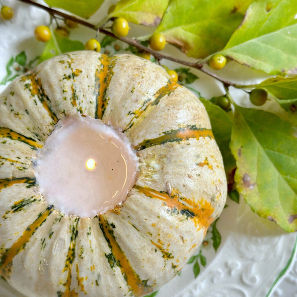 A top view of the candle burning in the pumpkin. these is a small branch of yellow berries and green leaves next to it.