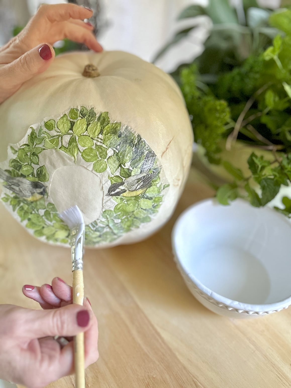 A wreath that is green leaves and 2 birds from a napkin. this wreath is on the side of a white pumpkin with a paint brush with mod podge. 