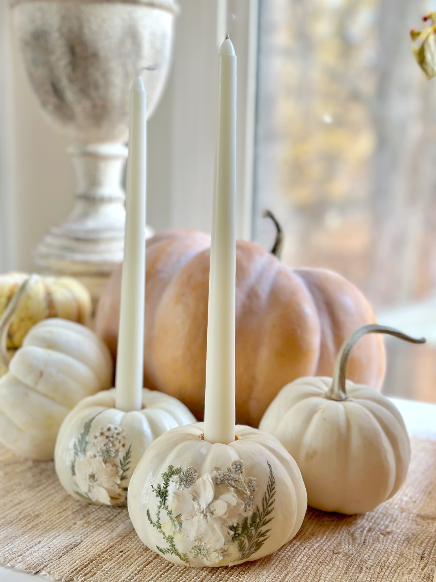 Two mini white pumpkins with pressed flowers on the front of them. They have taper candles in them.