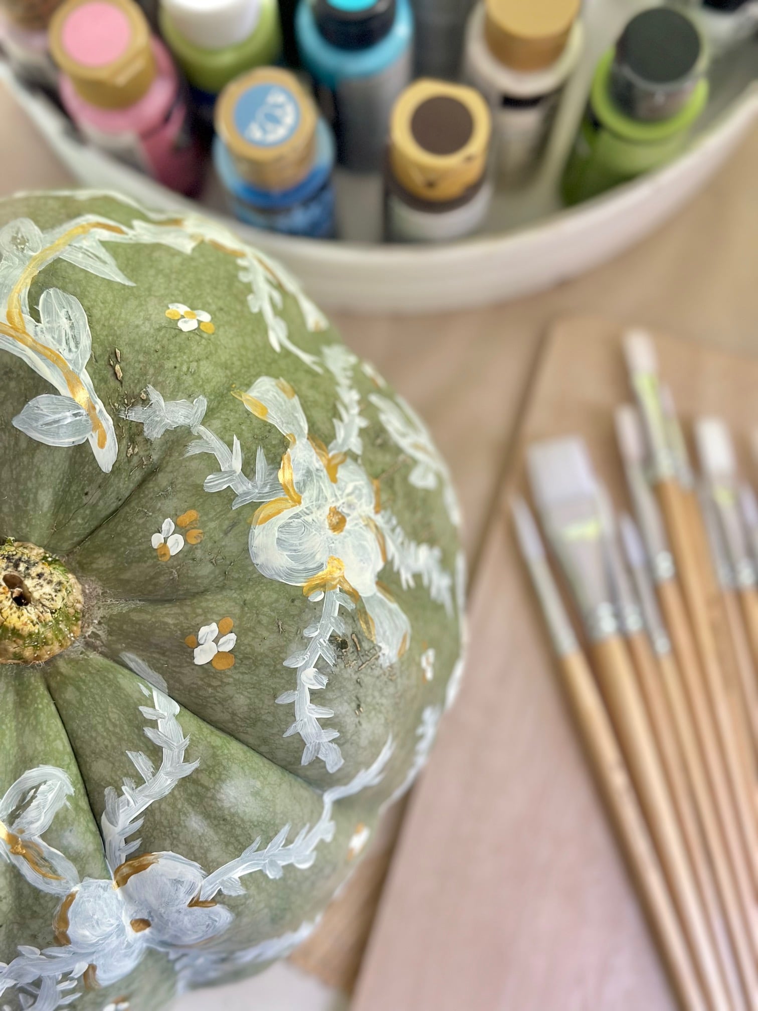 Green pumpkin painted with white vines and flowers.
