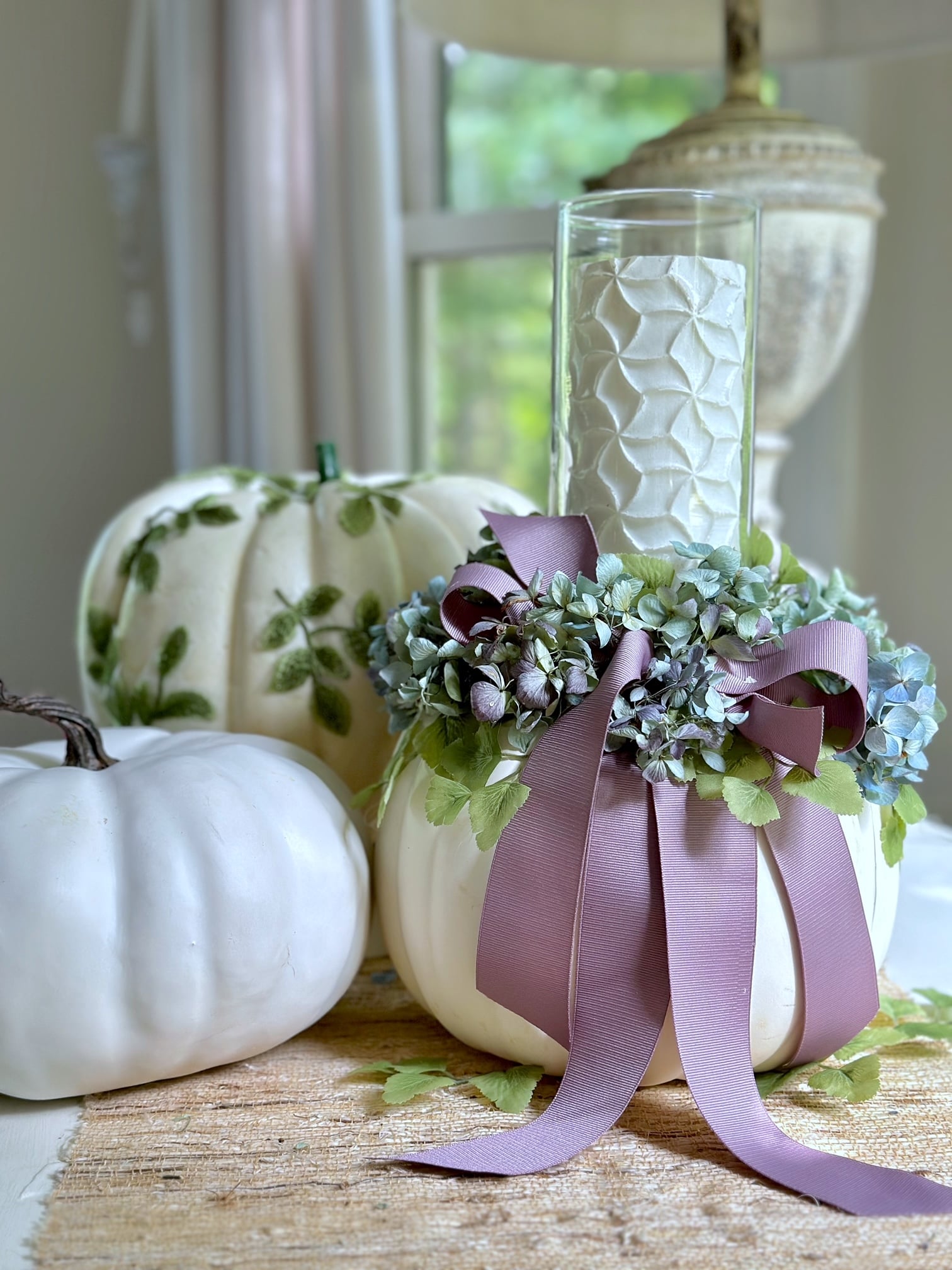 A white faux pumpkin with a glass vase with candle and dried hydrangea around the top.