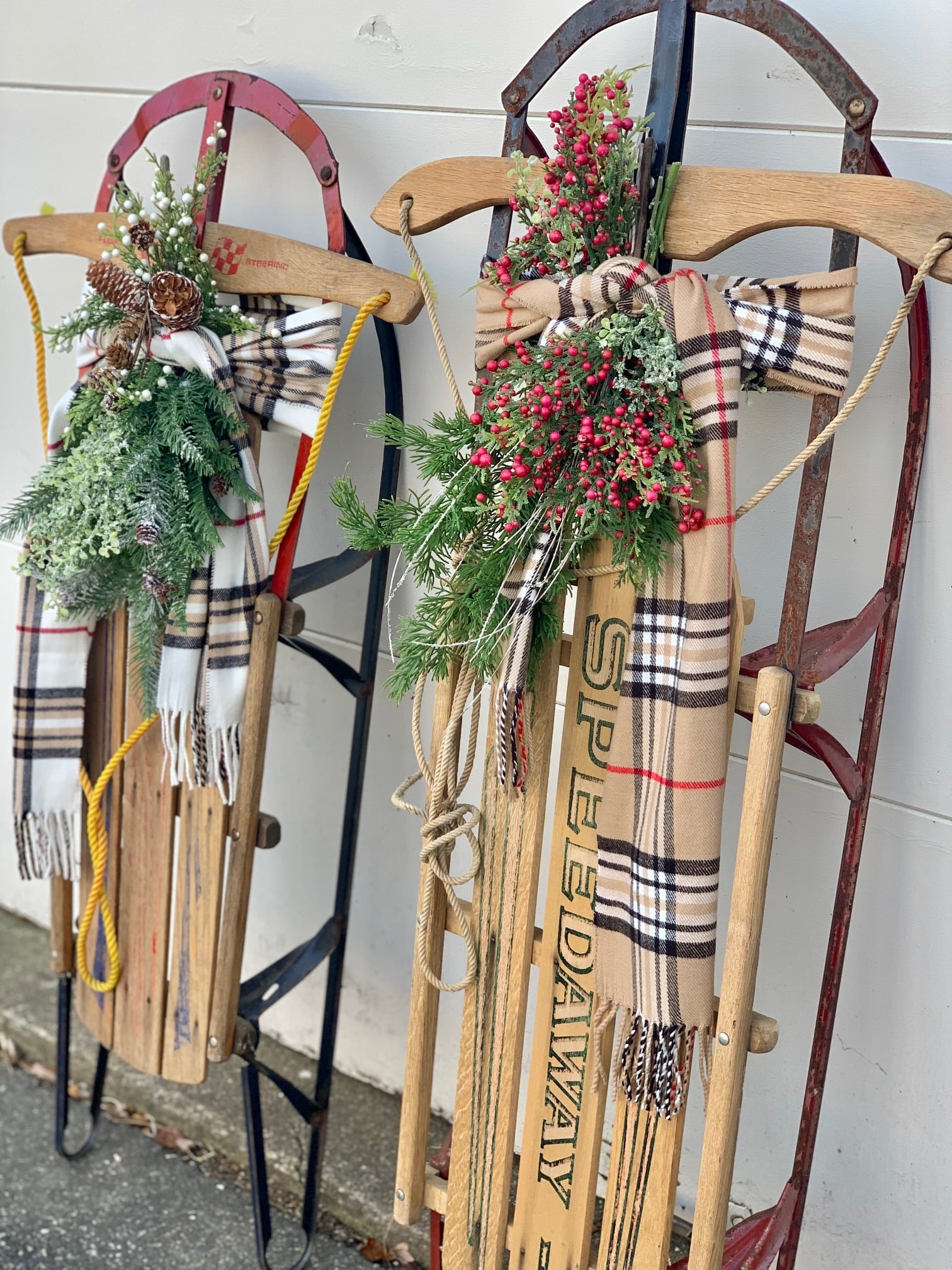 Two vintage wooden sleds outside with plaid scarves and swags of greens and berries.