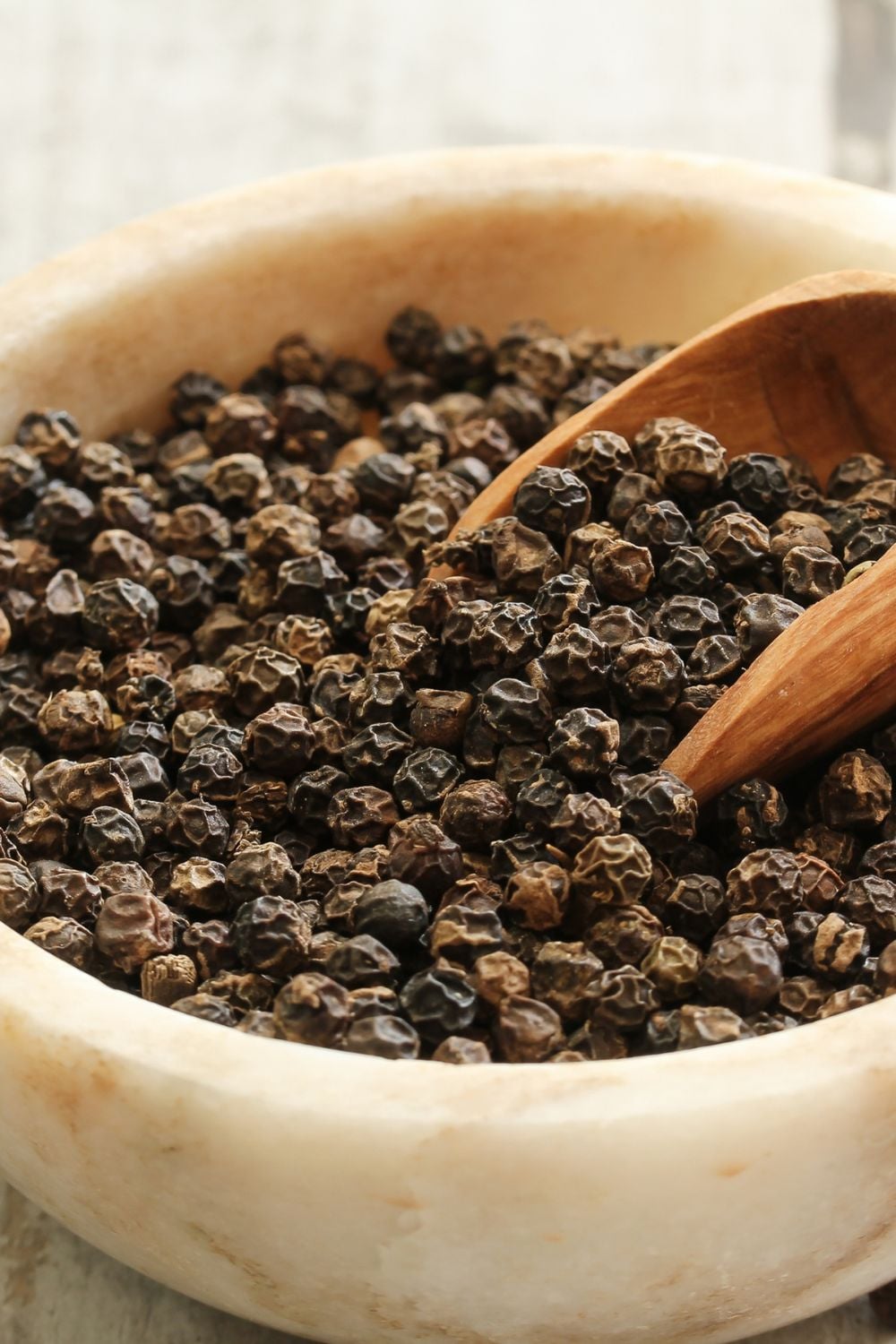 Black pepper in a wooden bowl with a scoop. 