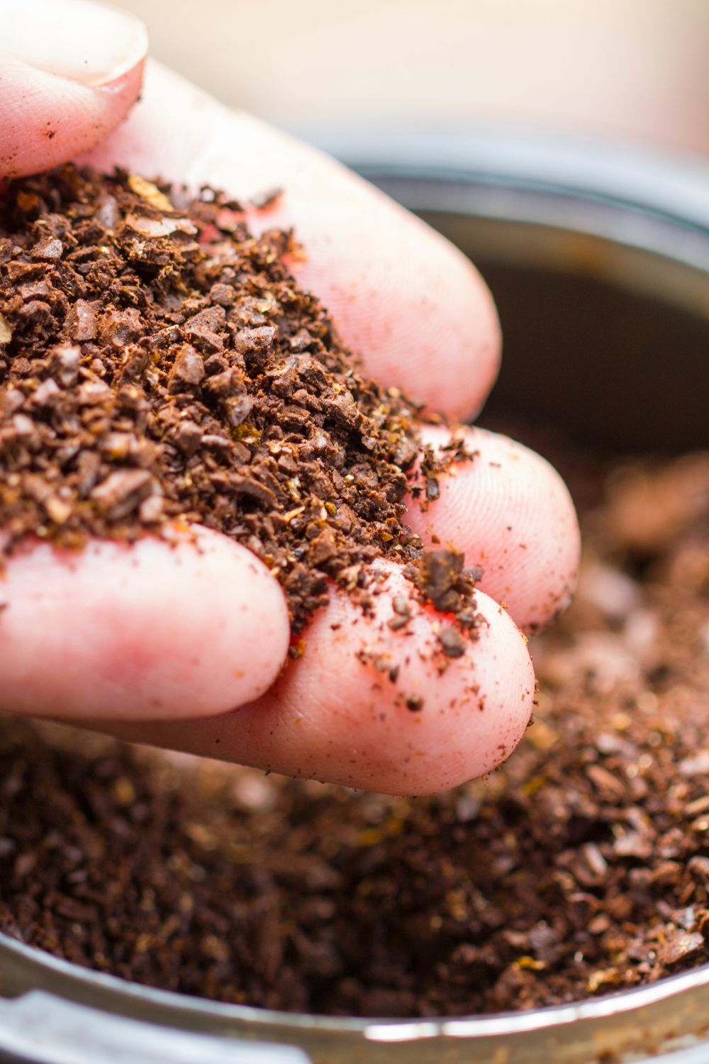 A hand holding coffee grounds that are stored in a jar.