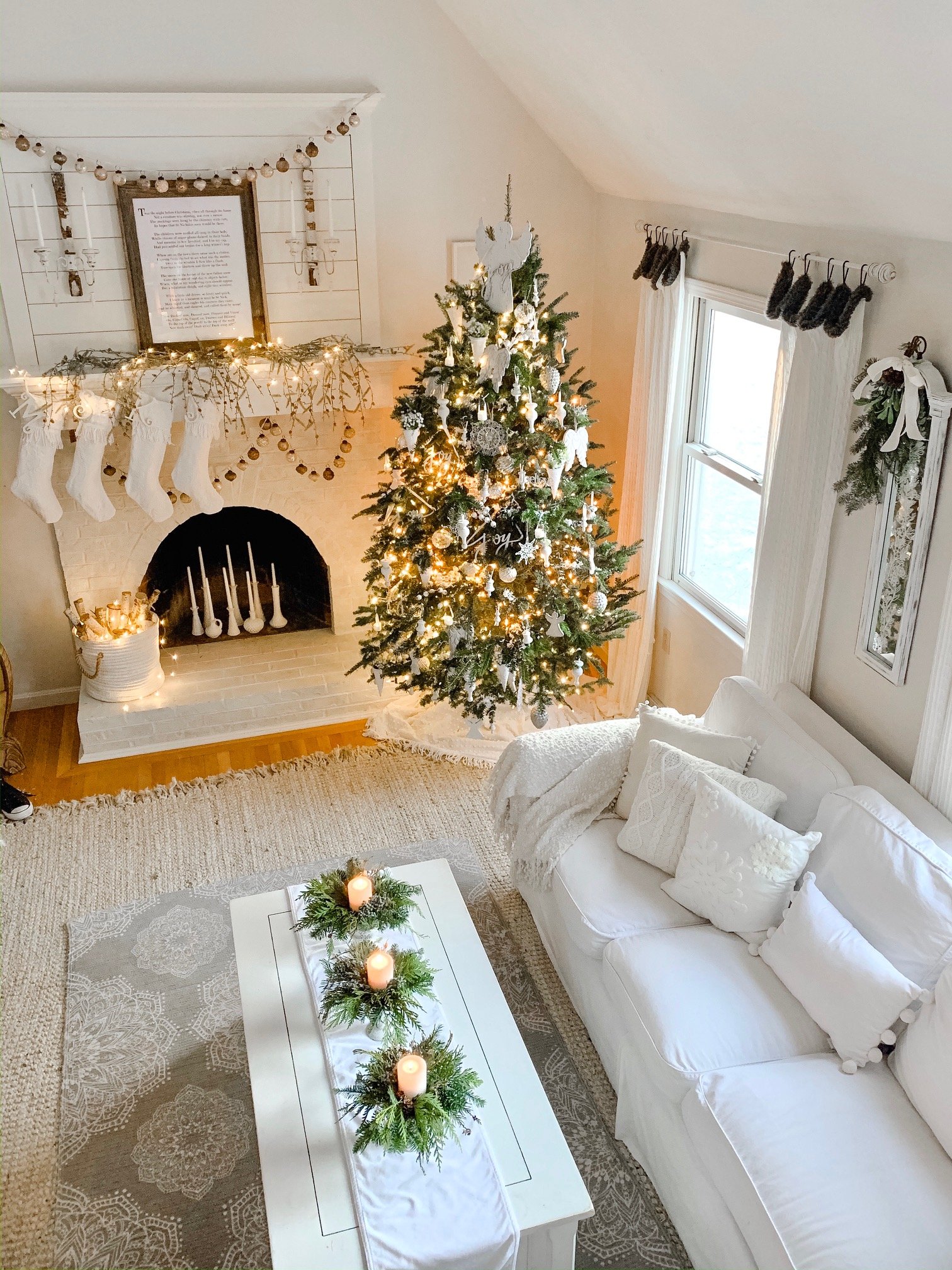 Cozy white living room during Christmas time with candles and a decorated Christmas tree.