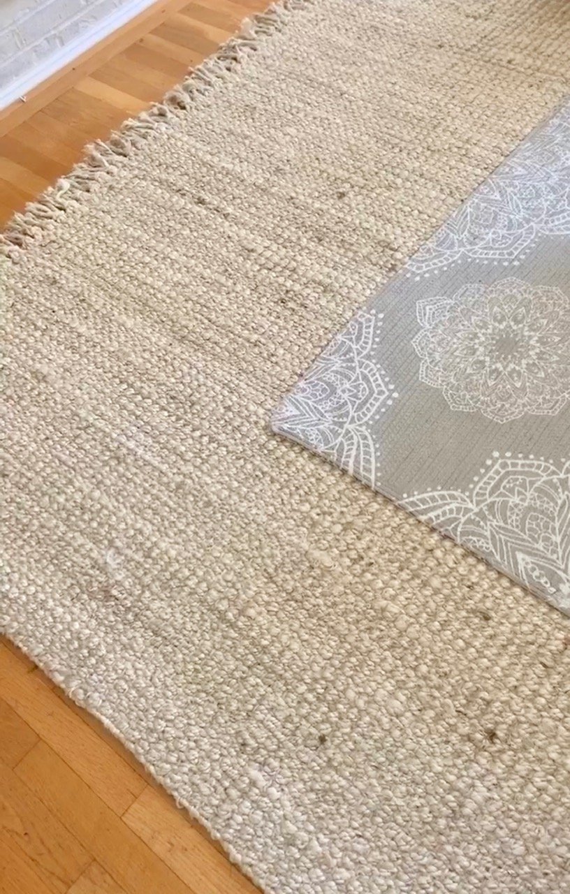 Close up of the two layered rugs. One is a thick jute rug is a soft sand color, the other is grey with a white design. 