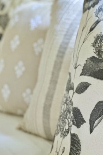 Four neutral throw pillows some florals, some stripes. Pillows are sitting on a white couch in a row.