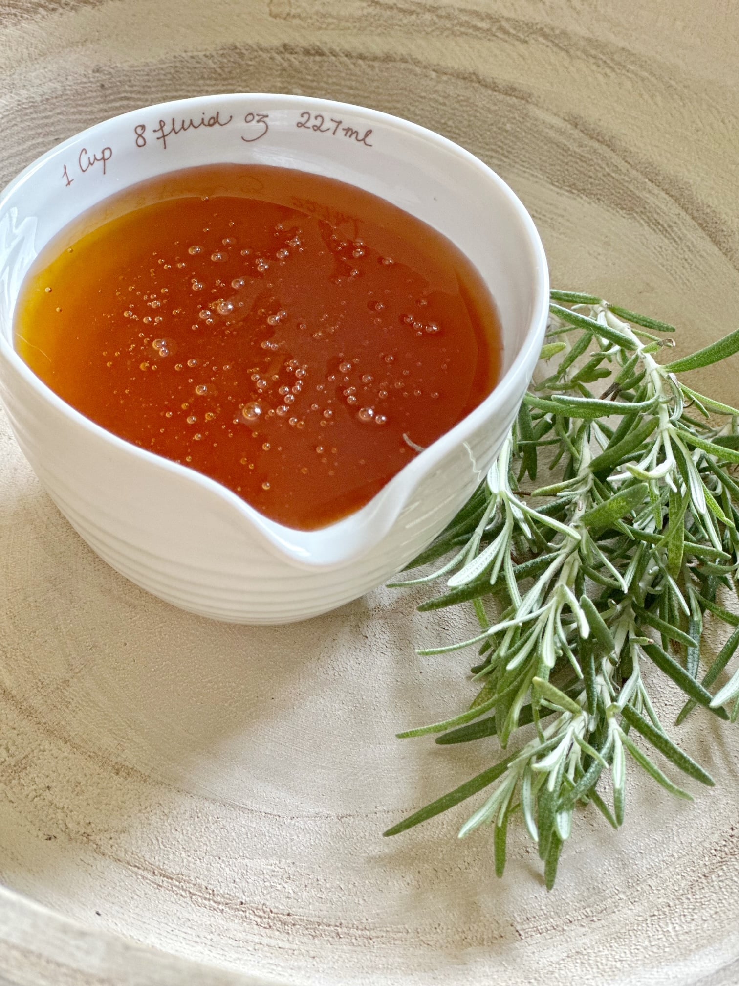 Cup of clover honey with a sprig of rosemary next to it. 