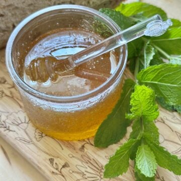 Mint honey in a glass jar with springs of fresh mint.