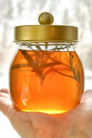Jar full of infused honey with rosemary sprigs in it.