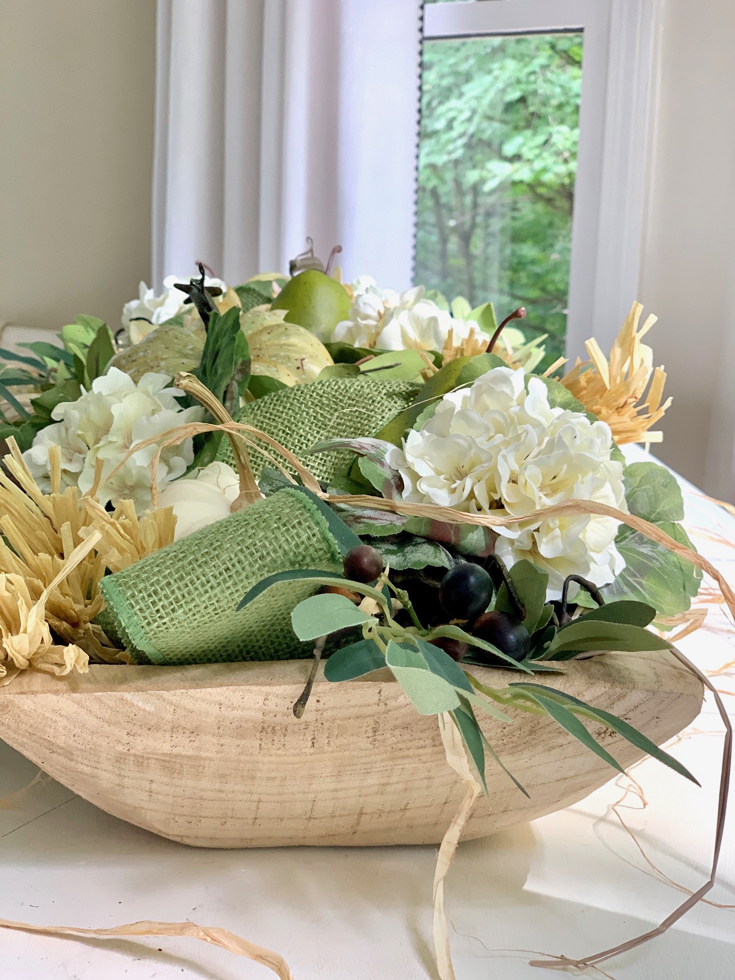 The completed dough bowl. In this image you can see the contents up close. There are olive branches, white blooms and green faux gourds.