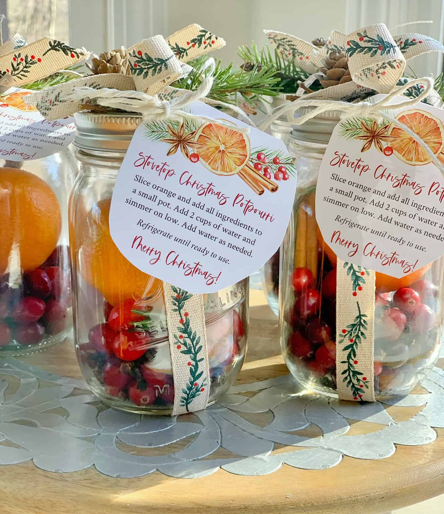 Gift jars filled with cranberries, cinnamon, oranges and rosemary. The jars are decorated with a bow and have a gift tag.