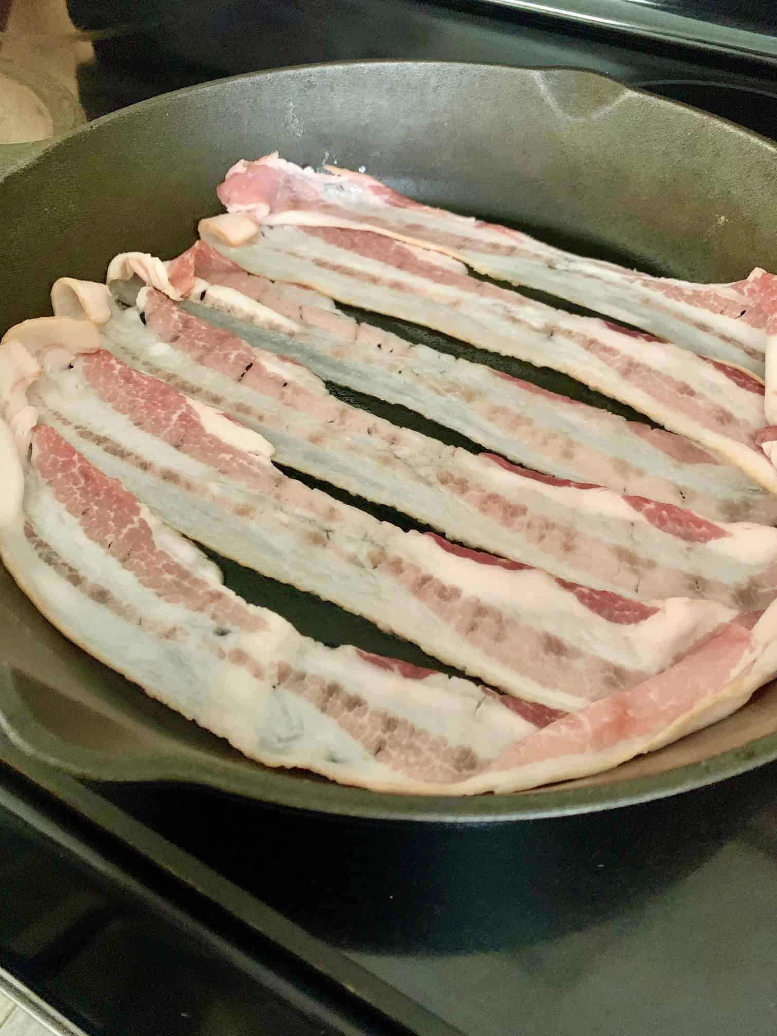 Bacon cooking in a cast iron skillet. 