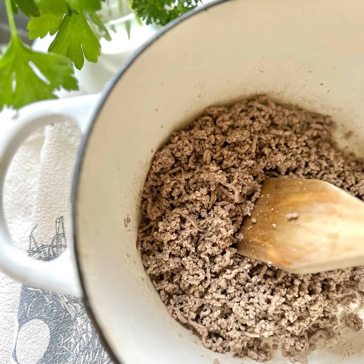 Beef being browned in a white pot. 