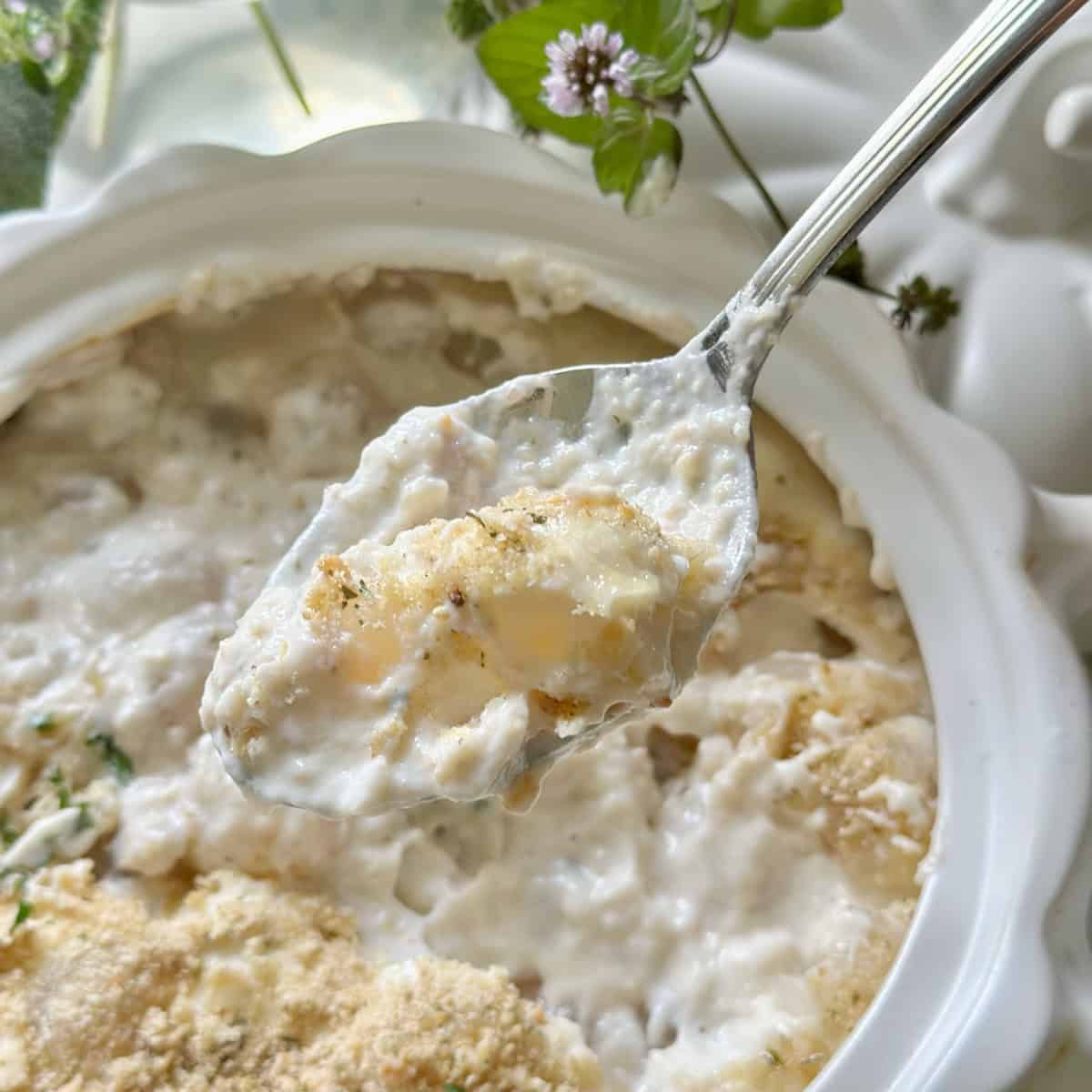 A forkful of creamy onions that have breadcrumbs, parmesan cheee and parsley on it.
