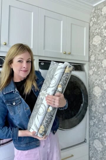 Me standing in my laundry room holding several different rolls of wallpaper options.
