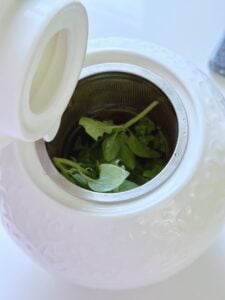 A tea pot with fresh herbs.