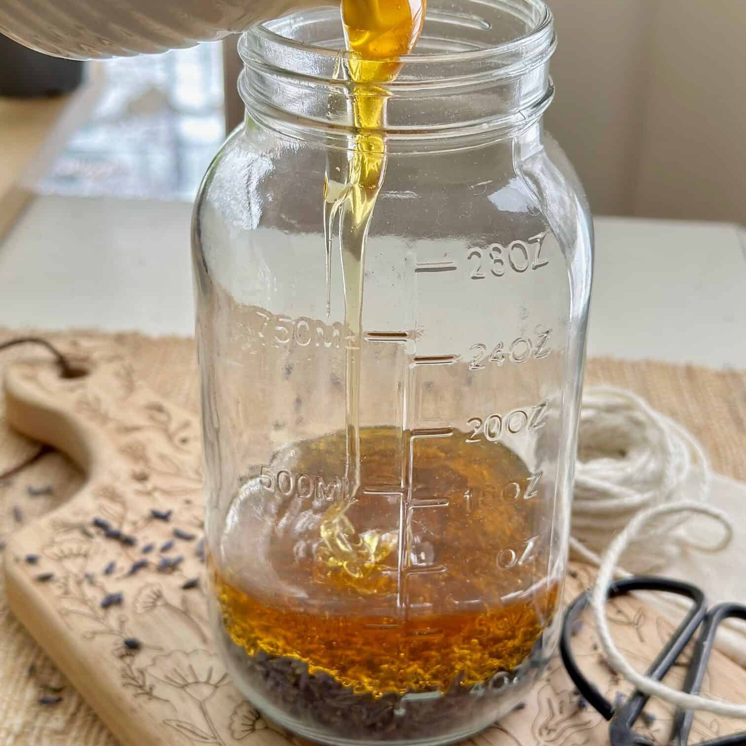 Pouring honey over lavender in a clear glass jar. 