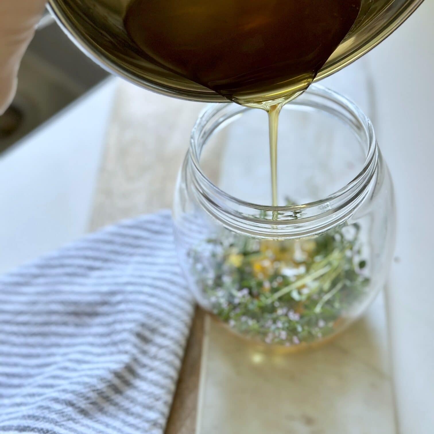 Pouring the warmed honey into the jar with thyme stems. 