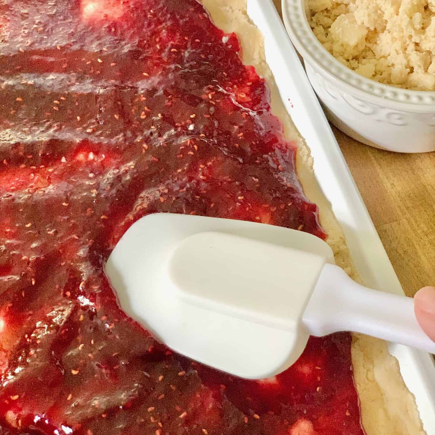 Spreading prepared raspberry jelly over the pressed dough. 