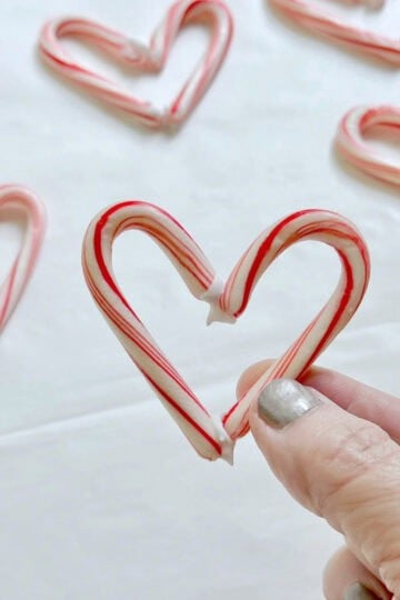 Me holding a mini candy cane heart in front of others that are drying. These hearts are fully edible, no glue or baking needed.
