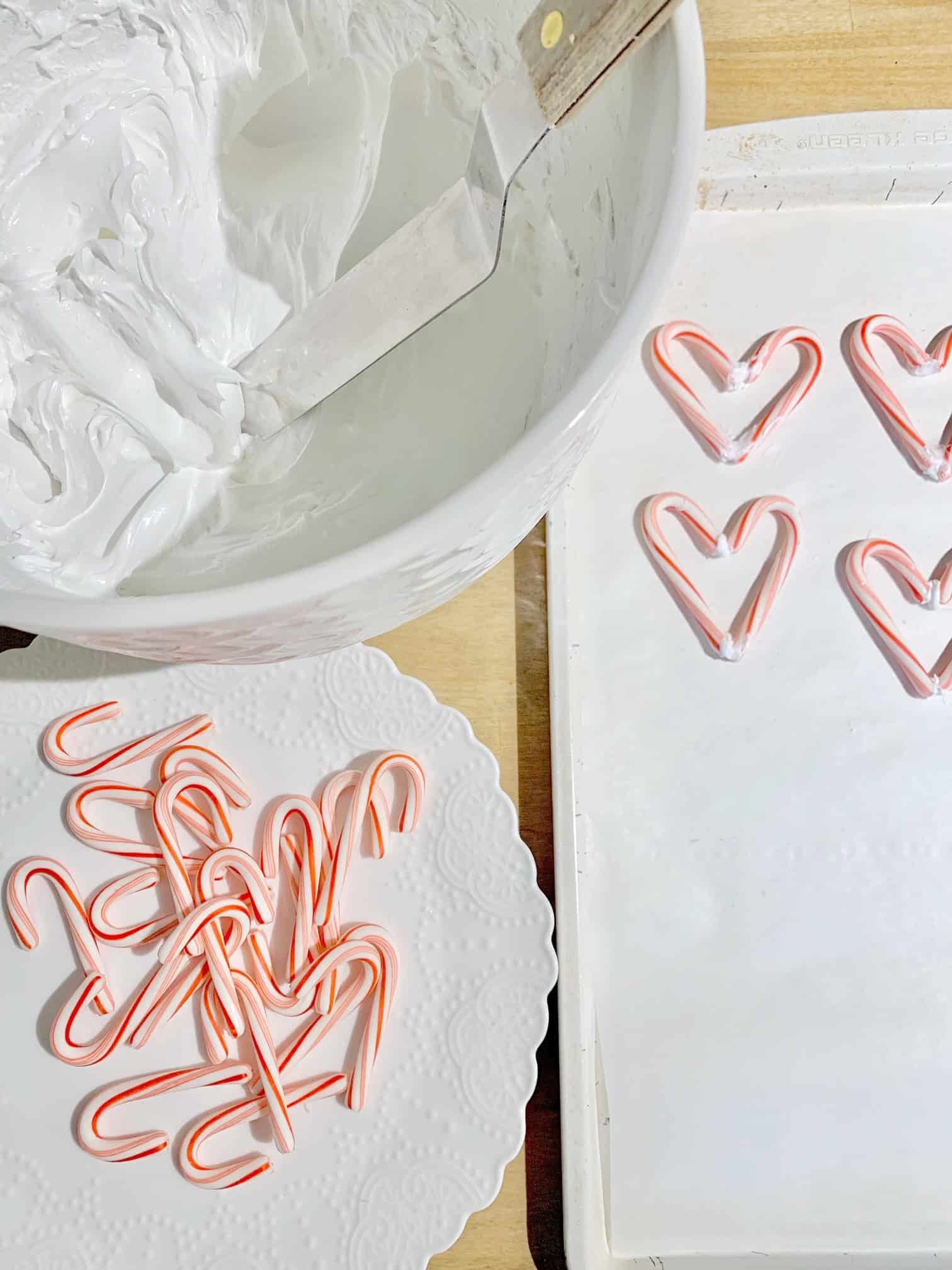 A large white mixing bowl with mixed meringue, small candy canes and candy cane hearts. 